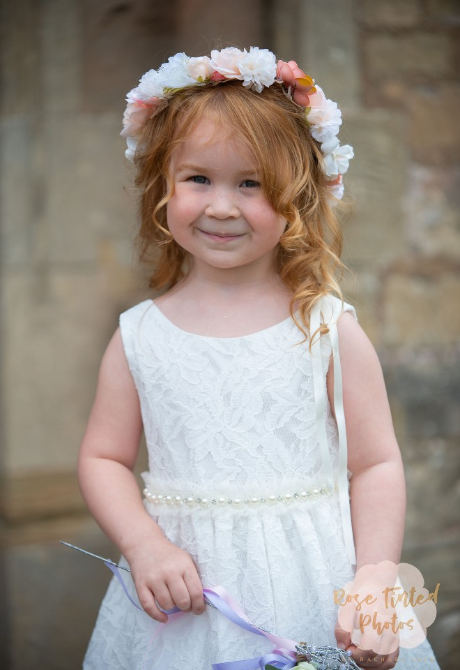 Young flower girl smiles at the camera outside the church as she awaits the arrival of the bride