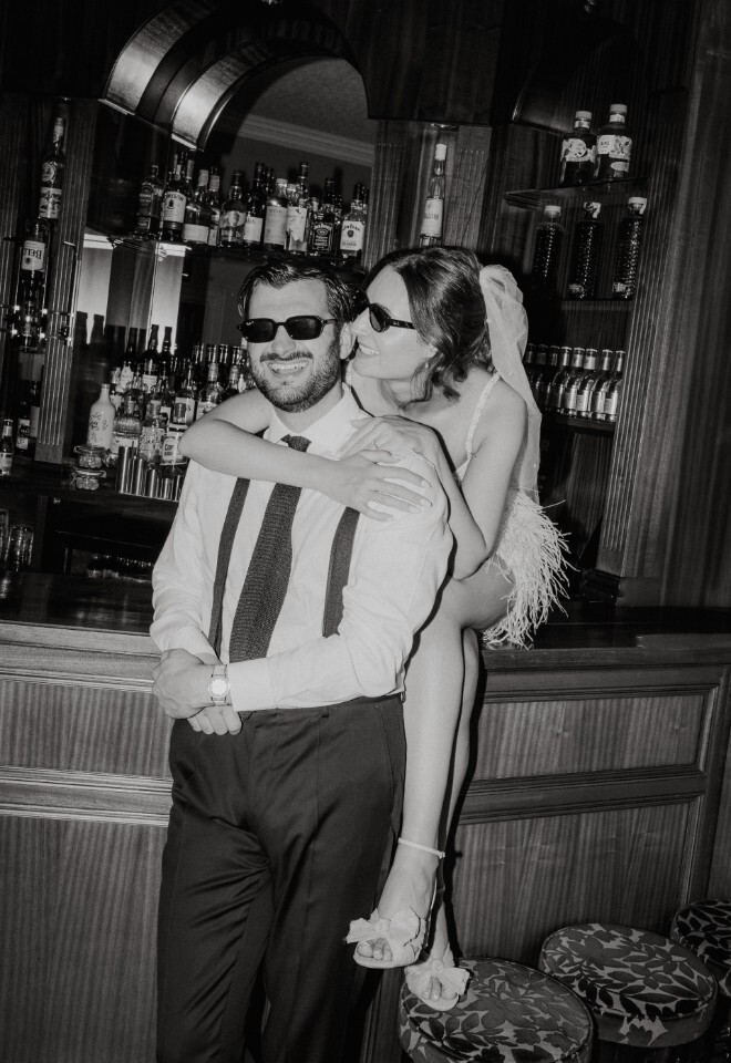 Stylish black-and-white shot of a bride and groom in sunglasses at a bar, laughing together in chic, modern wedding attire at Washingborough Hall Hotel.