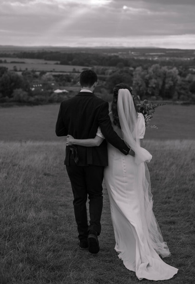 A bride and groom walk down a hill hugging.