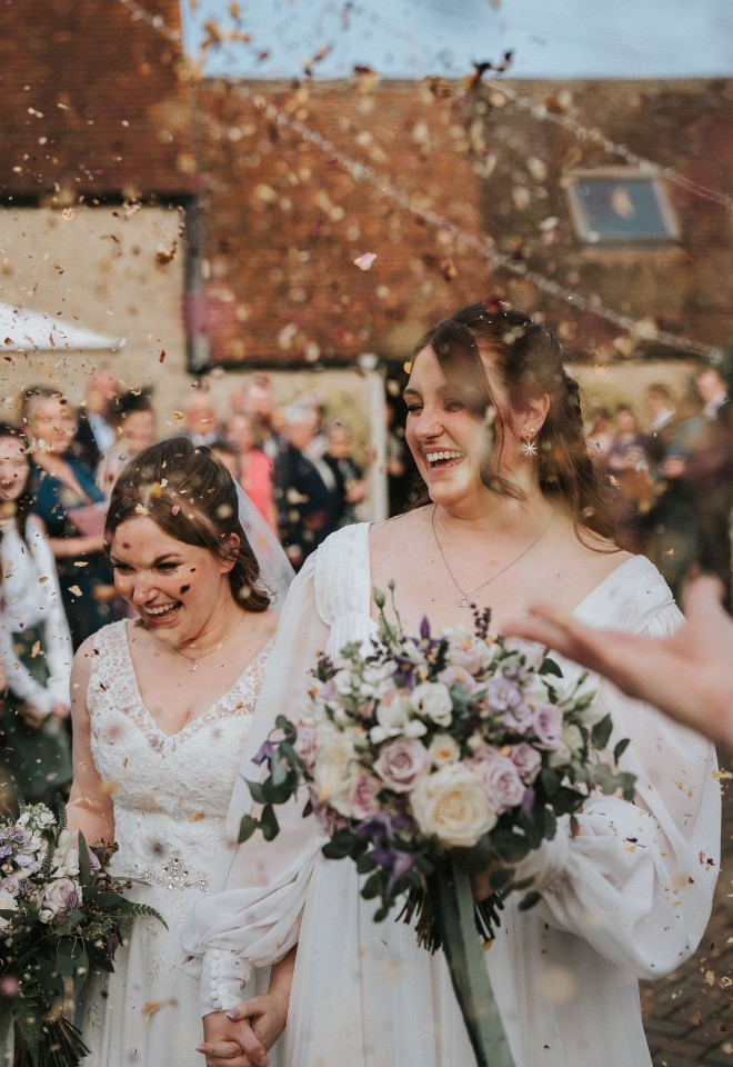 Confetti shot of two brides in the courtyard of a lovely oxfordshire barn wedding venue