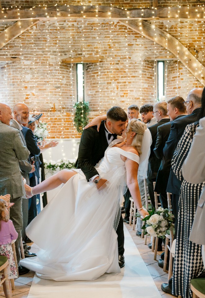 Dip kiss on the ceremony exit in the 17th C barn. Ball gown with leg slit, tux, white and green wedding