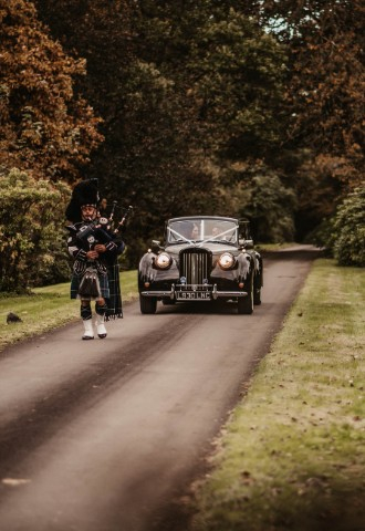 Piper leading wedding car at Auchen Castle - a romantic castle wedding venue in Scotland
