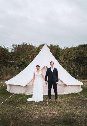 A bride and groom hold hands in front of a yurt