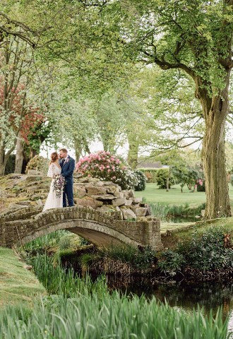 Bride and groom pose on a bridge in the grounds of Colshaw Hall, Cheshire