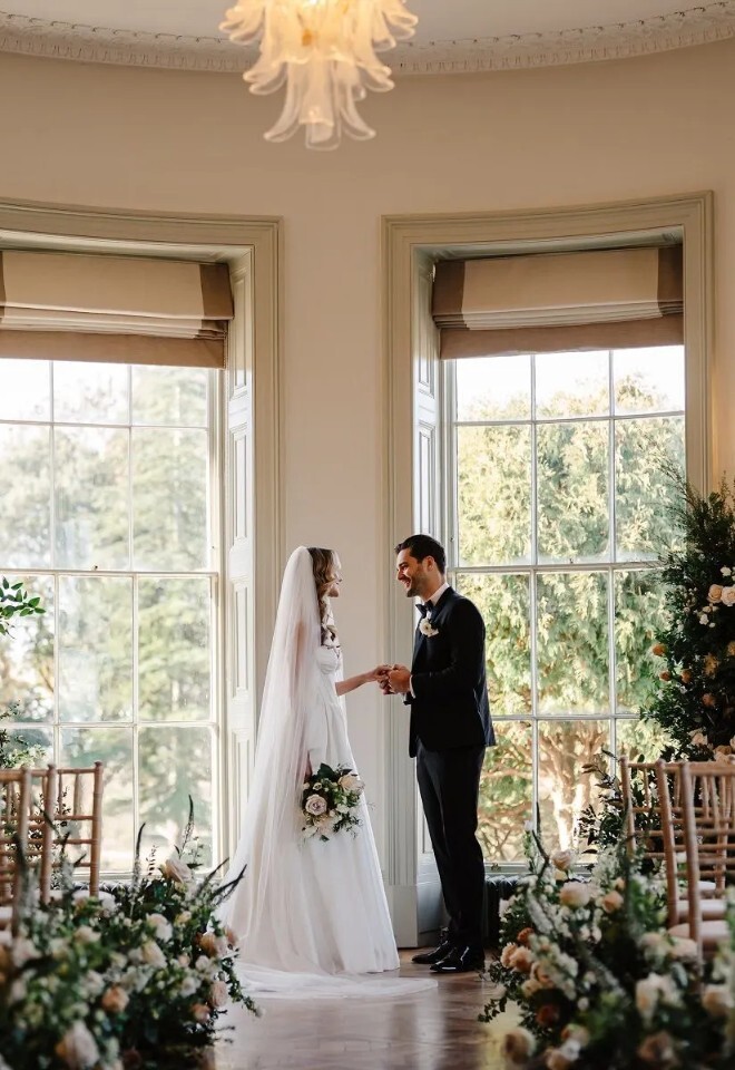 Bride and groom embracing beneath the sweeping staircase at Henlade House wedding venue in Somerset, showcasing classic interiors.