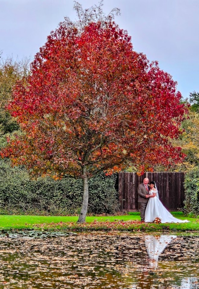 A couple stood under a gree near the lake at Yarlington Barn in the Autumn