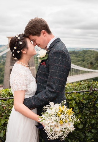 Newly married couple embracing in front of the Clifton Suspension Bridge