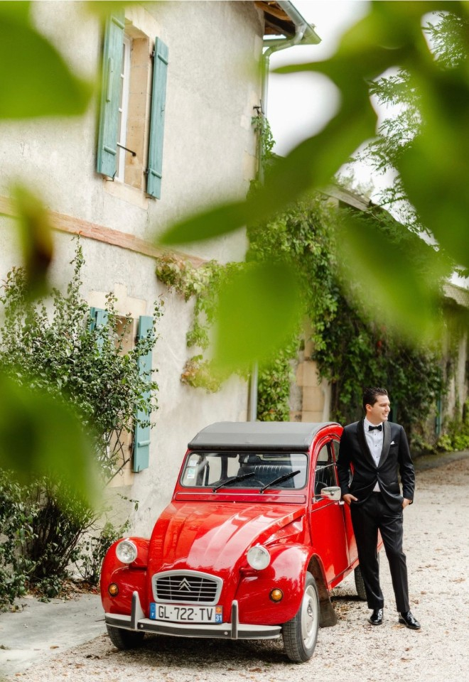Citroën 2CV red wedding car with groom stood next to it waiting to marry at Chateau de Saint Martory in France