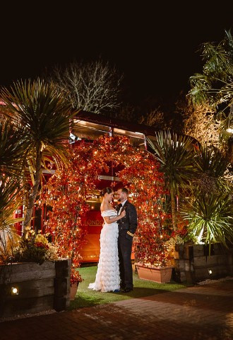 bride and groom pose by the big red bus outside the crazy bear, stadhampton, oxfordshire