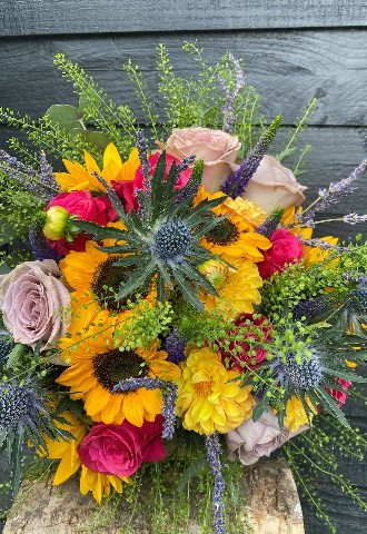 a bridal bouquet made up of roses, sunflowers dahlias and thistle all in shades of yellow, purple and pink by ann laing flowers in harwell oxfordshire