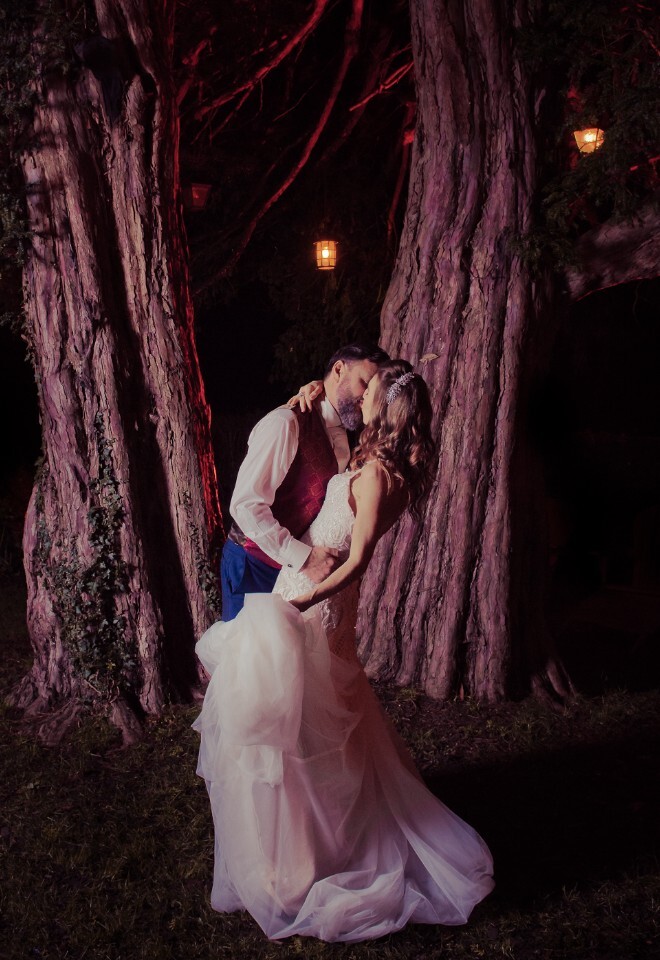 Bride and groom kiss under a lantern lit tree on the evening of their wedding