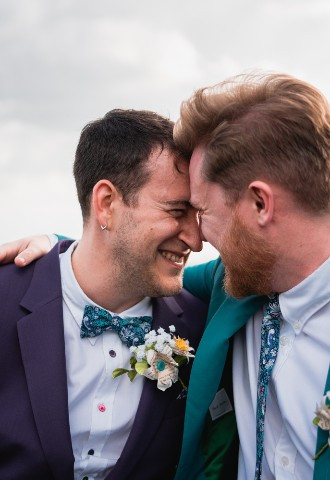 Two newlywed grooms embrace and laugh on their wedding day