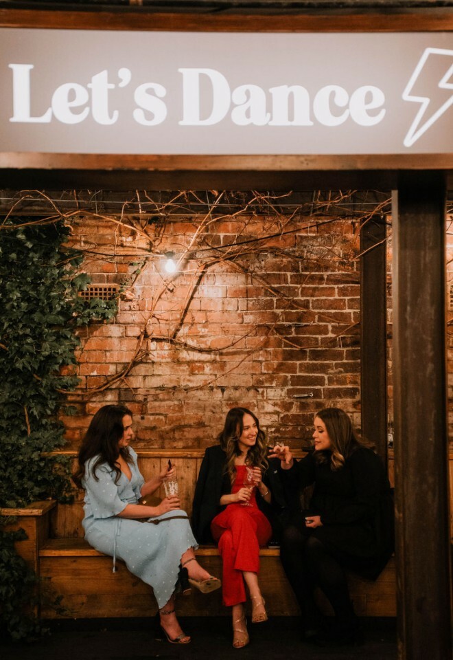 Guests sat under lets dance lightbox sign at night