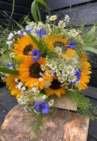 a bridal bouquet made of sunflowers, daisies and cornflowers with grasses and foliage by ann laing flowers, harwell, oxfordshire