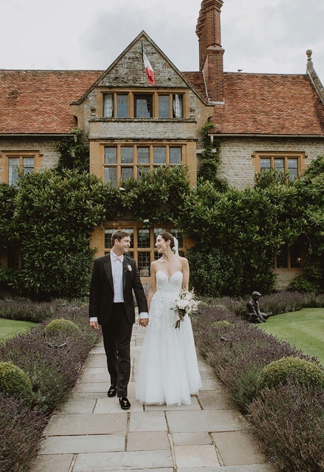 Bride and groom walking hand in hand through the gardens of a historic Oxfordshire wedding venue, captured naturally by V & H Photography.