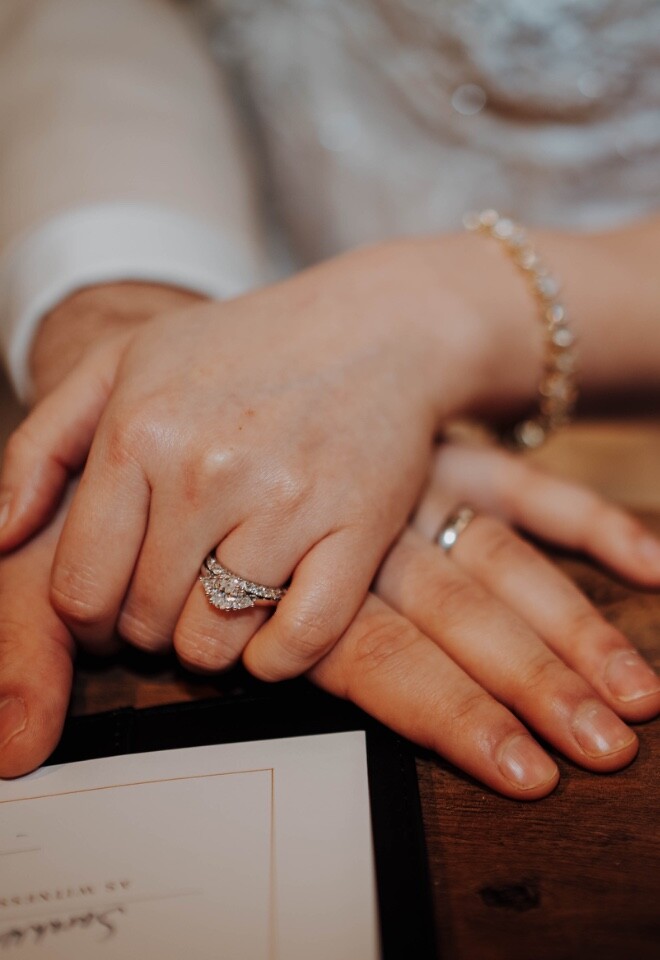 Man and woman on their wedding dat at their wedding ceremony holding hand with their wedding rings and engagement ring after signing register