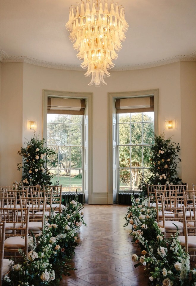 Light-filled ceremony room at Henlade House wedding venue in Somerset, styled with floral-lined aisle and wooden chairs.