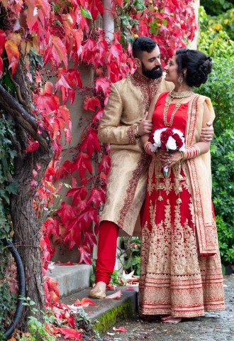 Bride and groom next to wall of red leaves