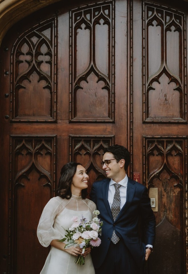 Newly married couple standing together in front of large wooden doors at an Oxford college, photographed by V & H Photography