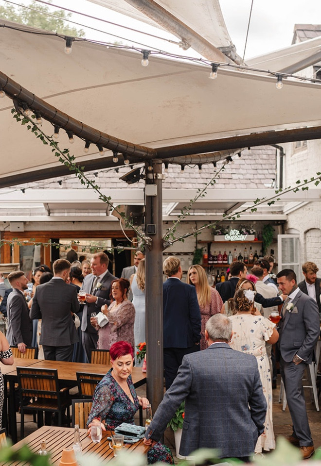  Wedding guests enjoying a relaxed drinks reception in the courtyard at The Cock O’Barton.