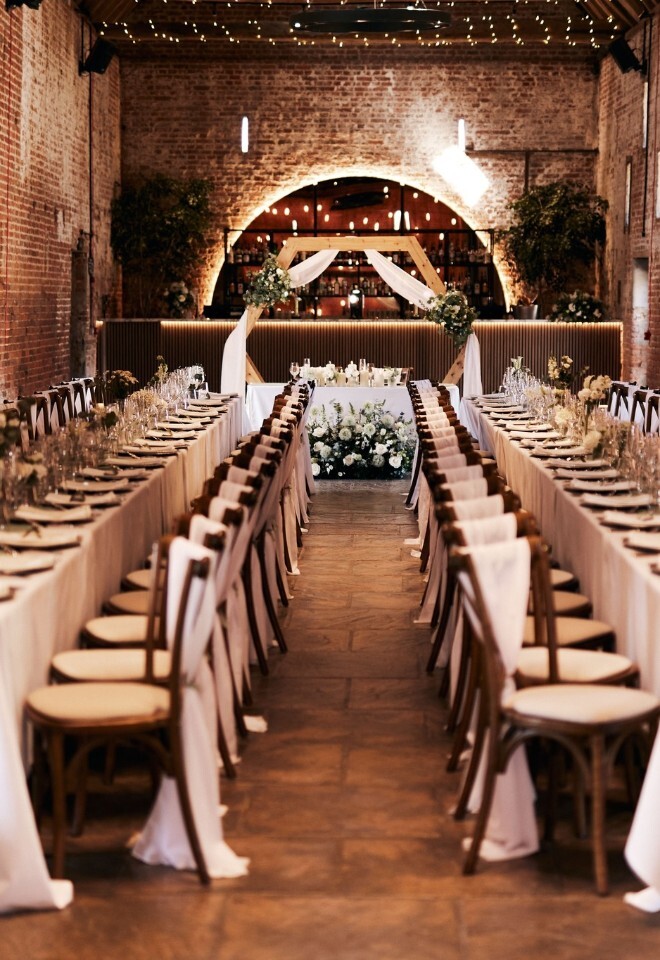 Sweetheart table and tressel tables set for a wedding reception in the barn at Copdock Hall