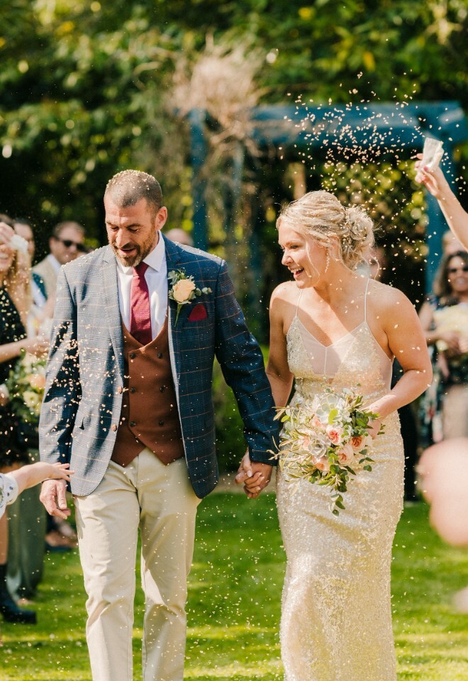 Bride and groom in garden ceremony walking back down the aisle with confetti