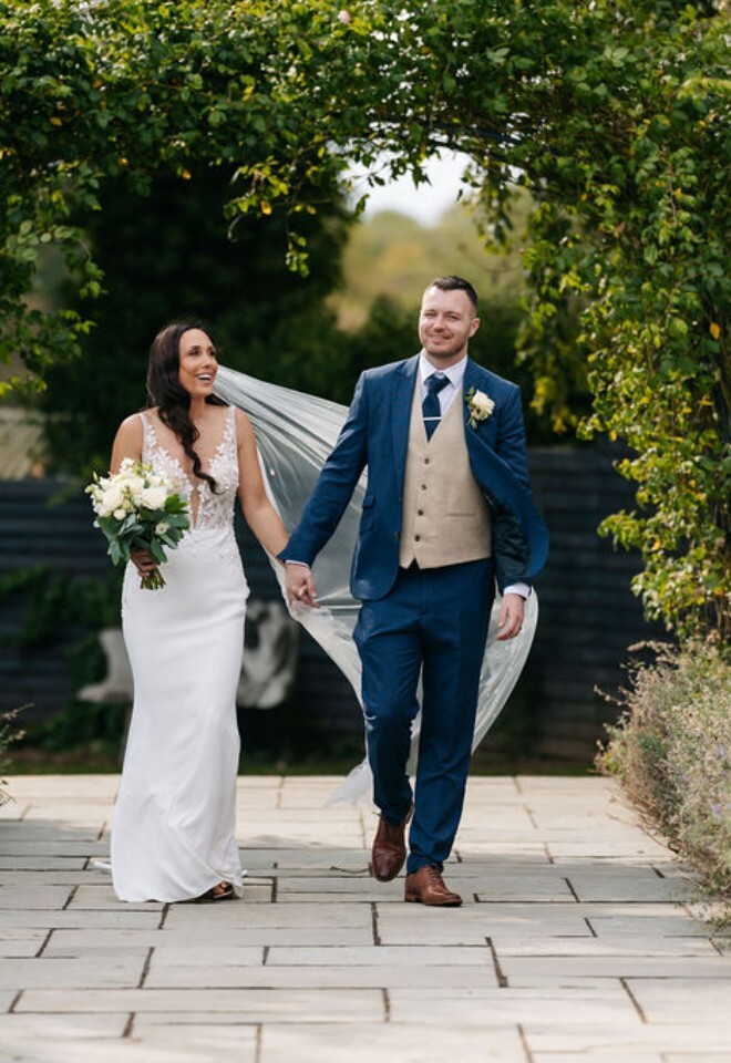 A bride and groom walking through the garden at an exclusive Warwickshire wedding venue