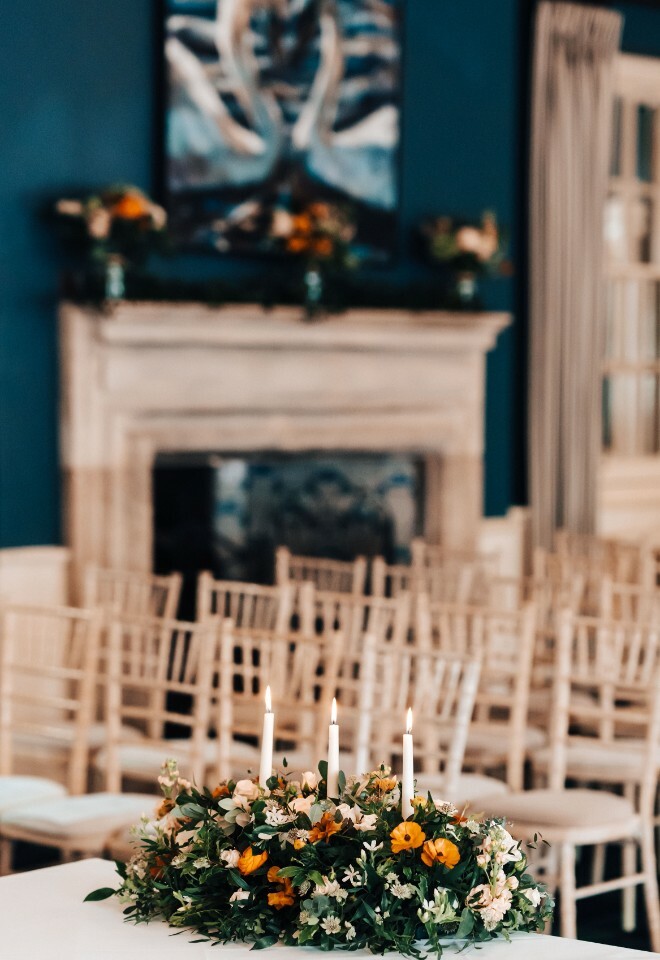 Wedding ceremony with flower arrangement with orange and white flowers. Three lit candles sit in the centre of the flowers