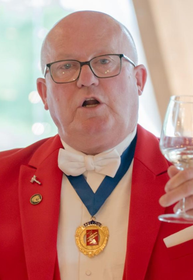 Surrey wedding toastmaster and celebrant Toastmaster John raising a glass while hosting a wedding reception in his traditional red tailcoat.