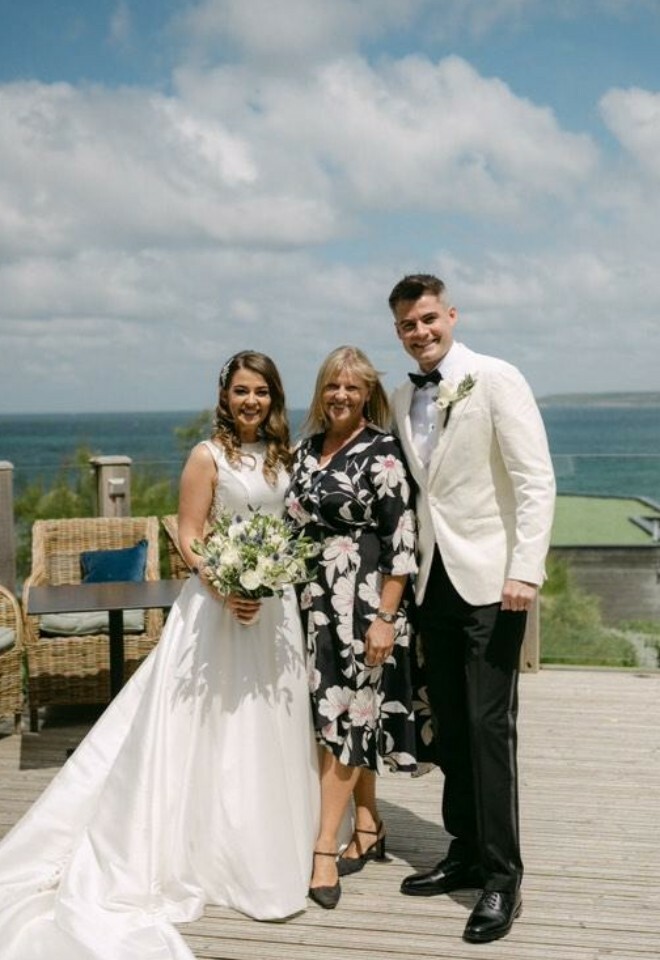 Celebrant with married couple standing on hotel decking near beach