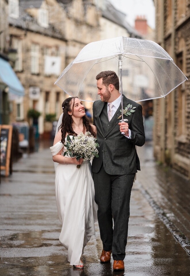 Bride and groom walking through Cirencester in the rain on their wedding day.