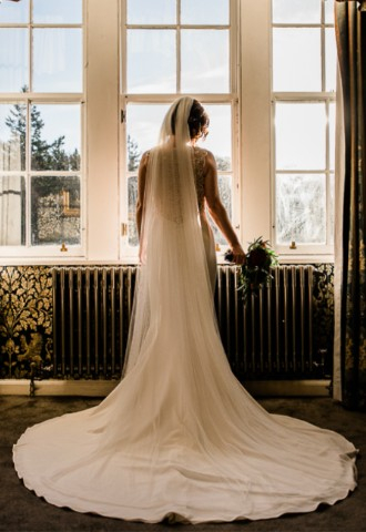 Bride looking out suite window down at wedding guests on patio at Melville Castle - a castle wedding venue near Edinburgh