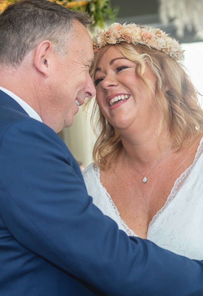 Candid moment between wedding couple sharing laughter under tree canopy.