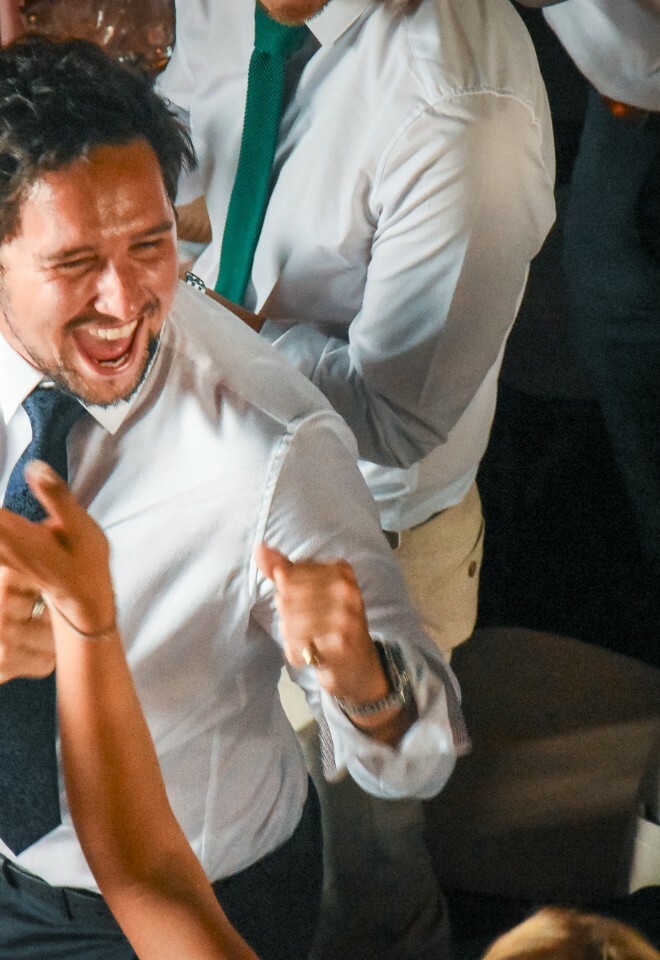 An excited individual in business attire celebrates enthusiastically with a crowd at what appears to be a social gathering.