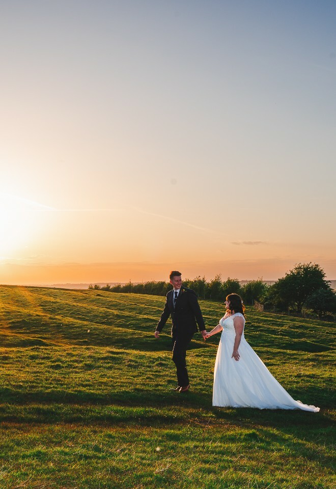 bride and groom walking across fields at sunset