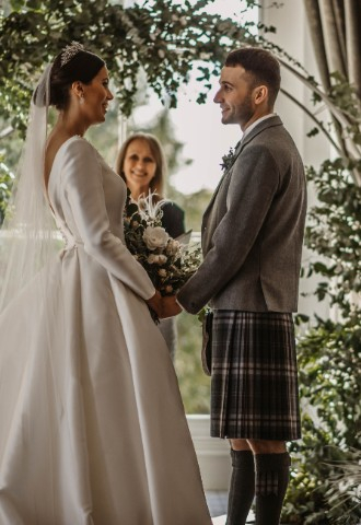 Bride and groom surrounded by flowers saying wedding vows at Auchen Castle - a romantic castle wedding venue in Scotland
