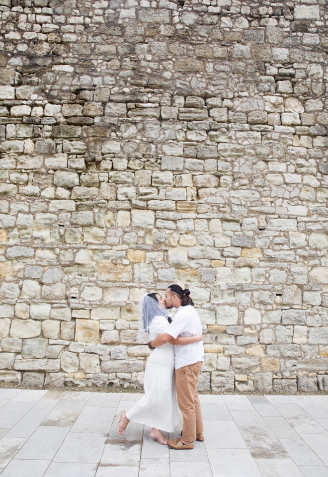 a young couple kiss on their walk along the old town walls towards the registry office for their intimate wedding ceremony. 
