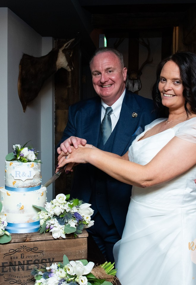 Bride and Groom cut into a white wedding cake adorned with fresh flowers and blue ribbons at the Woodsman Restaurant in Stratford-upon-Avon 