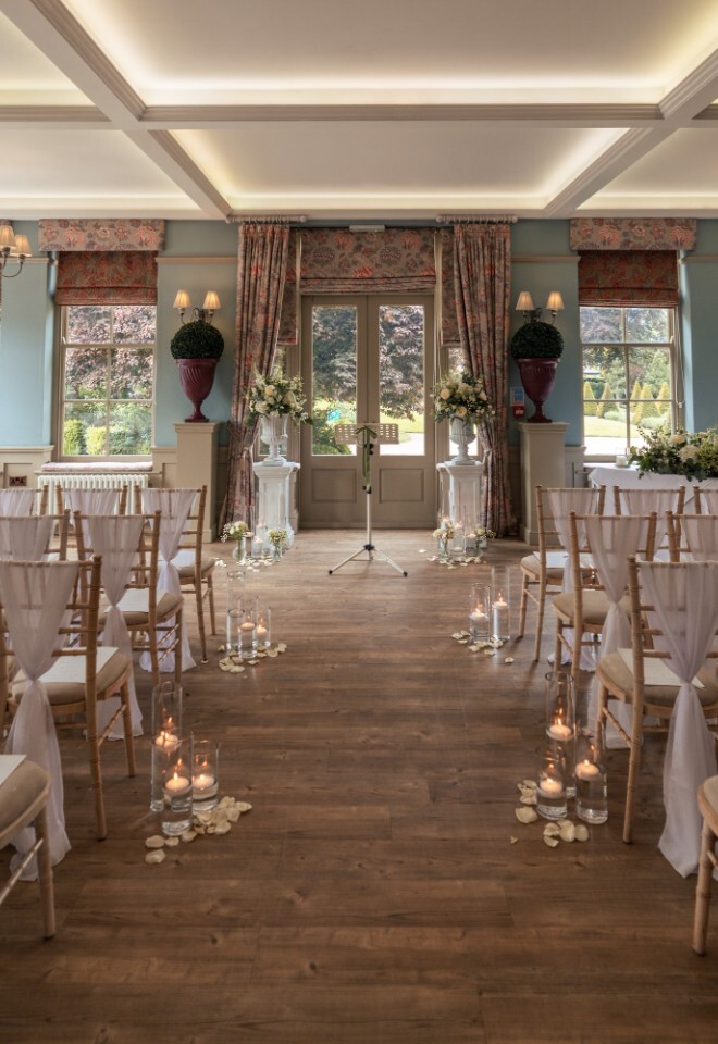 Ceremony room at Washingborough Hall Hotel set for a wedding, with rows of white-draped chairs, candles lining the aisle, and floral arrangements at the front.