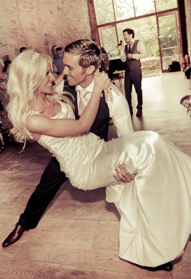 Groom lifts bride during first dance with wedding guests around while Matt Cardel sings 