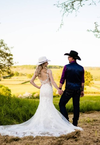 Bride and Groom, both wearing stetsons,  hold hands whilst looking at each other, back ground of beautiful countryside hills