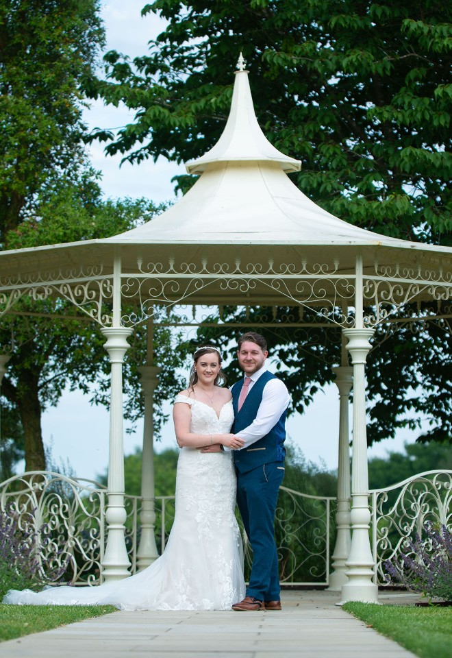 A bride and groom hold each other under the gazebo at Norwood Park Southwell on a sunny day