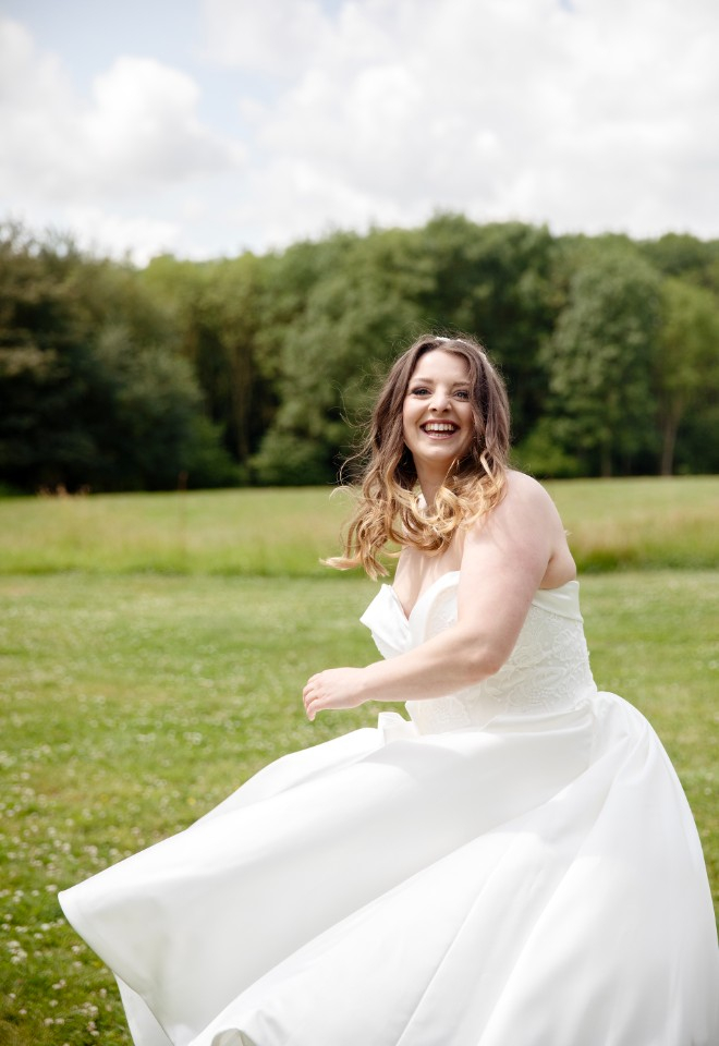 An excited bride swirls her dress and beautiful long curls in the wind at The Milking Parlor venue at Cavokay House