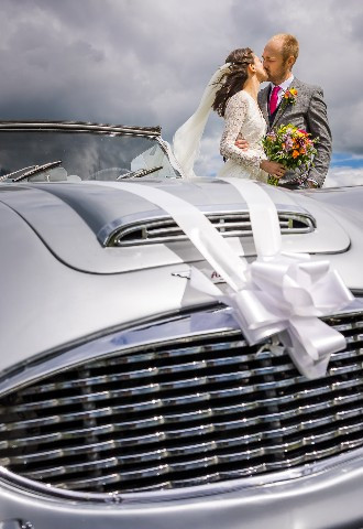 Newlyweds kiss next to their silver vintage wedding car