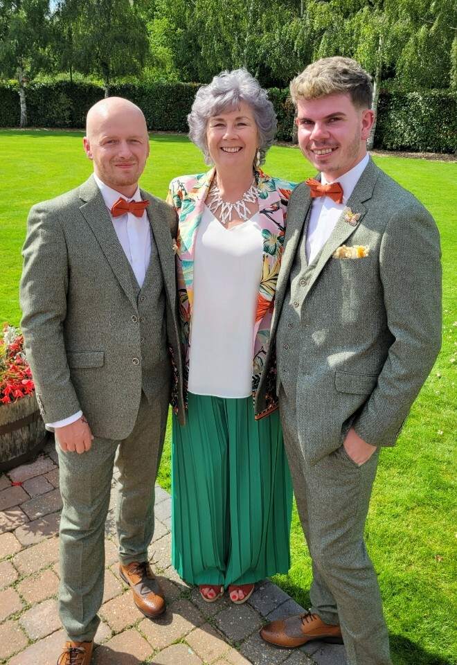 Essex Celebrant with two grooms after their wedding celebrant. They have sage green suits with terracotta bow ties and she has green trousers with a multi coloured jacket
