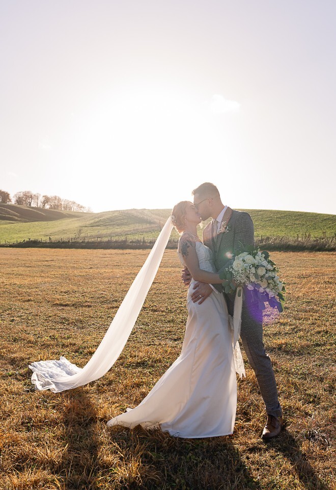 Bride and Groom kissing in a field at sunset at the Wellington Barn wedding venue