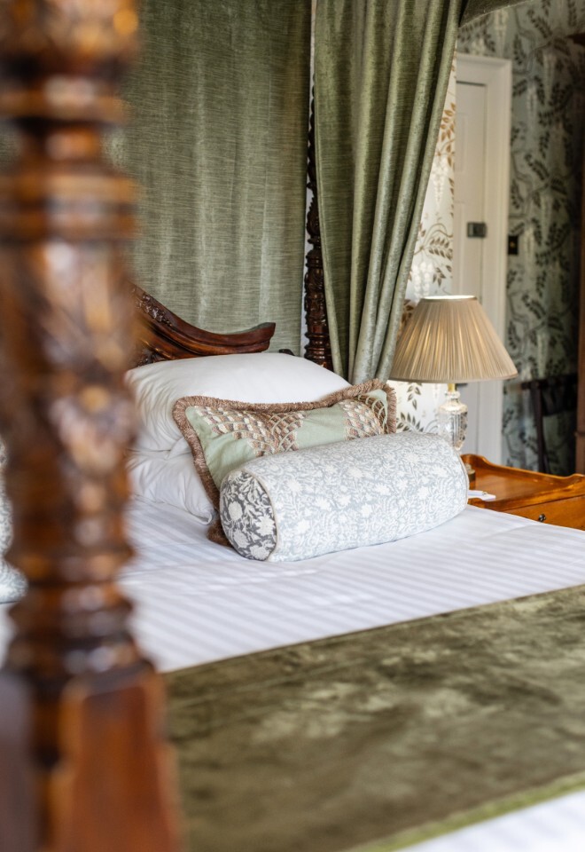 Bridal suite at Washingborough Hall Hotel featuring a carved four-poster bed with plush cushions, velvet drapes, and elegant patterned wallpaper.