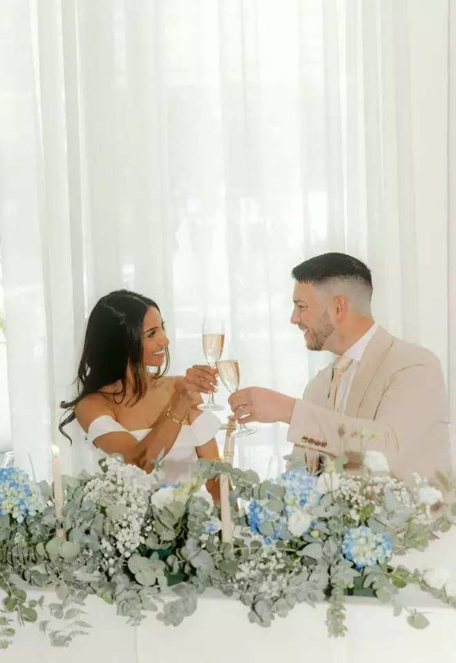 Bride & groom toasting their marriage at The Nici, Bournemouth, Dorset blue, white & sage green floral display at top table