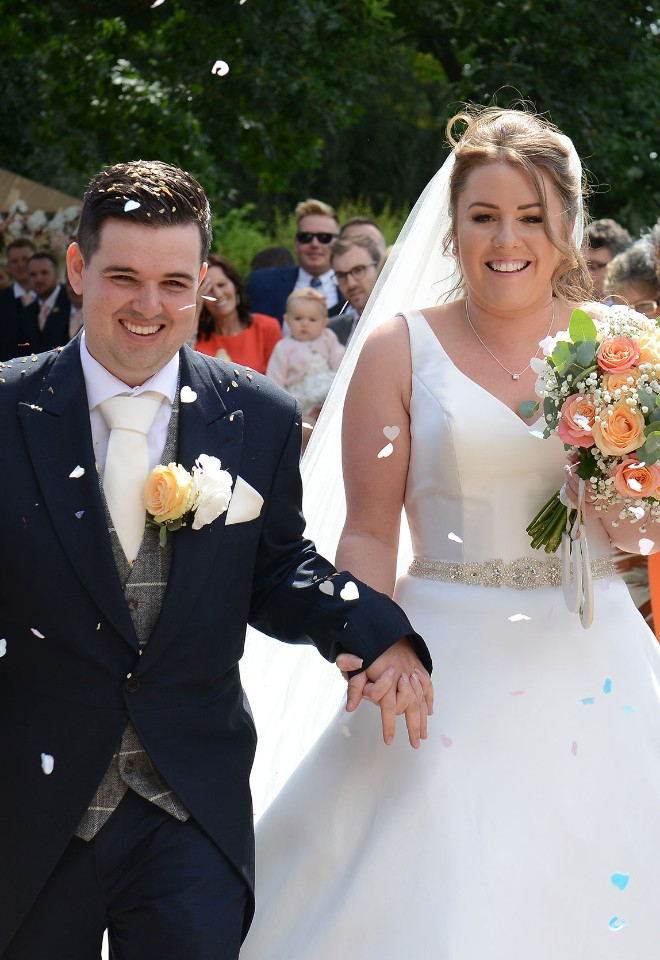 Newly married couple walk past their guests who shower them with white petal confetti at the outdoor wedding ceremony venue of Winstanley House, Leicester