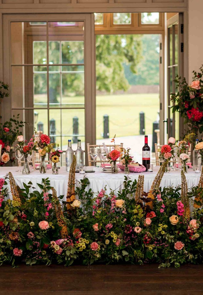 Meadow design in front of head table with bud vases above and deconstructed arch of bright spring flowers and foliage at Offley Place
